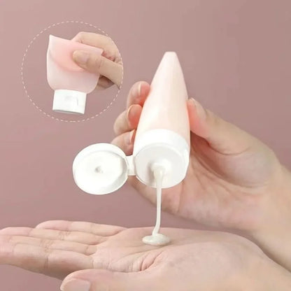 Hand holding a white cosmetic tube with pink cap, dispensing cream onto another hand against a pink background.