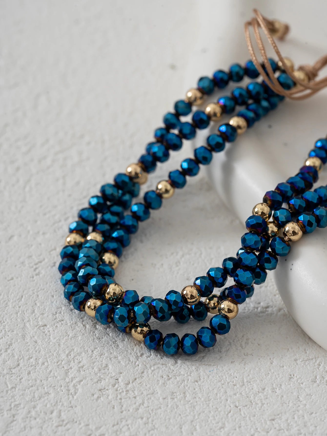 Blue beaded necklace with gold accents on a light gray surface