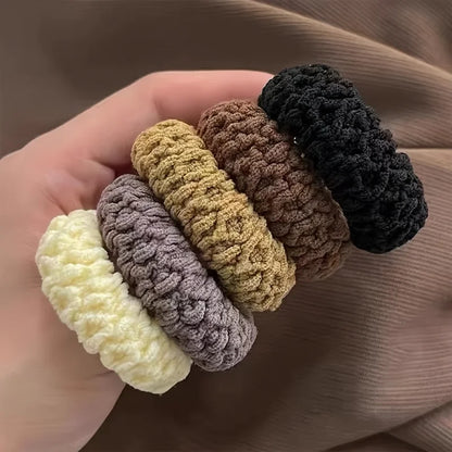 Set of five crocheted hair ties in various colors held by a hand.