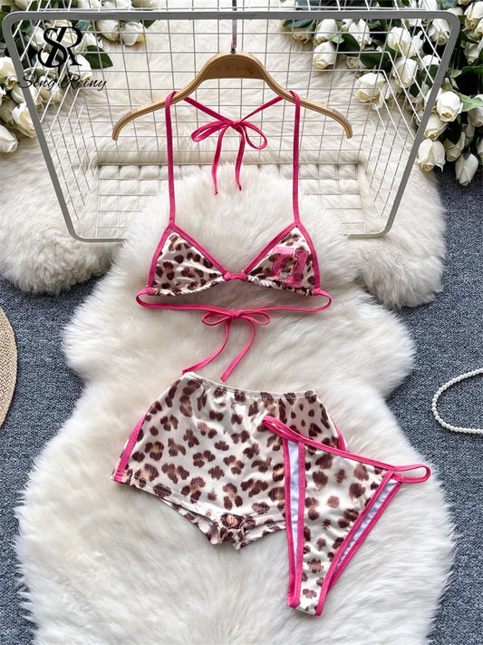 Leopard print bikini set with pink straps on a hanger against a textured white background.