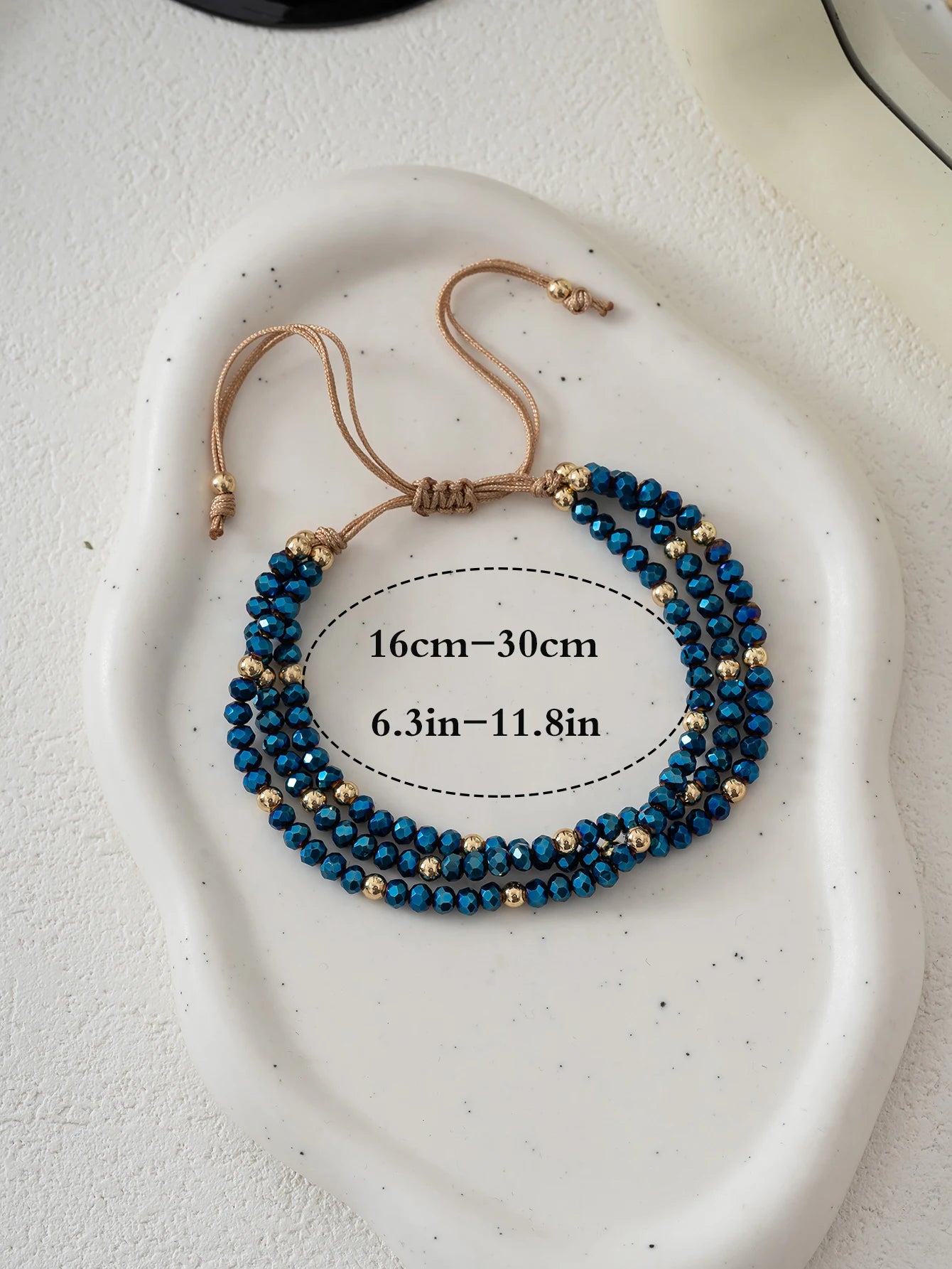 Blue beaded bracelet with gold accents on a white plate, showing measurement details.