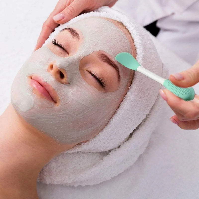 Person receiving a facial treatment with a towel on their head and a brush applying product.