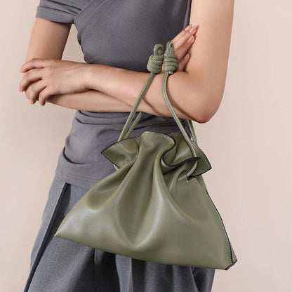 Person holding a green leather bag with a beige background