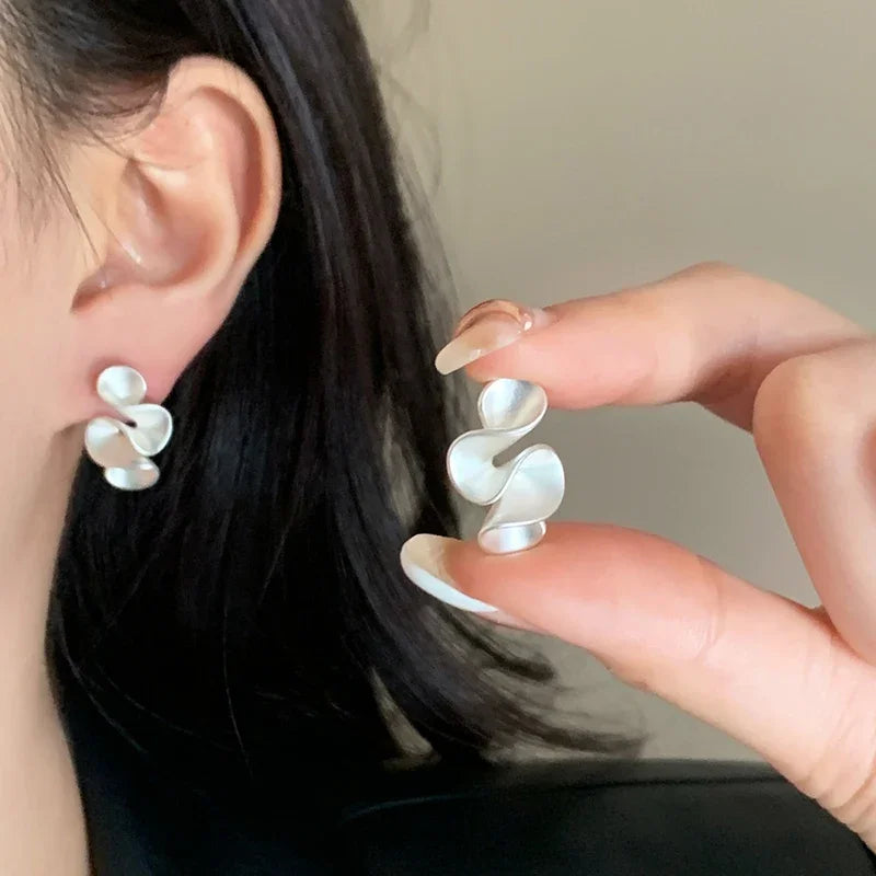 Person wearing a pair of white floral earrings with a hand holding one.
