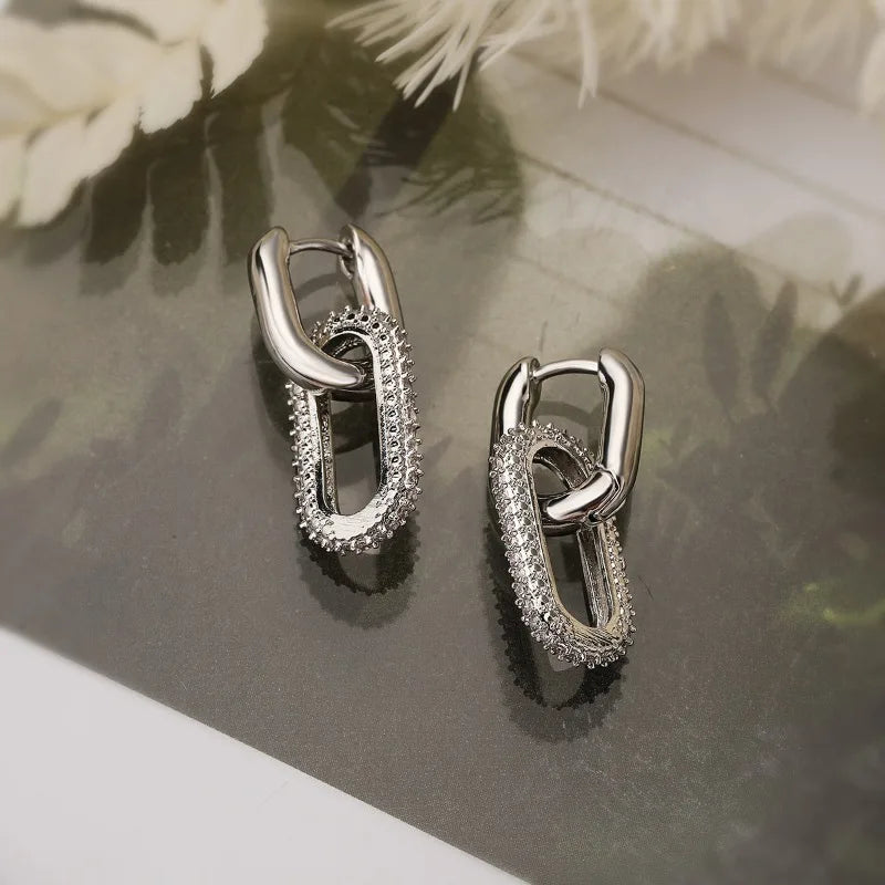 Pair of silver hoop earrings on a reflective surface with floral background