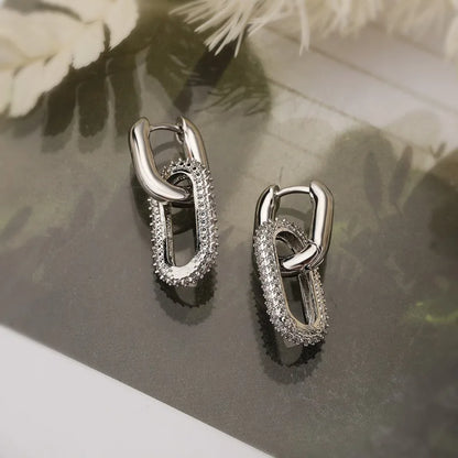 Pair of silver hoop earrings on a reflective surface with floral background