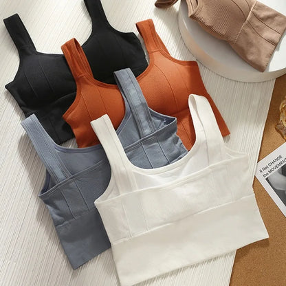 Set of four women's tank tops in black, brown, gray, and white on a textured surface.