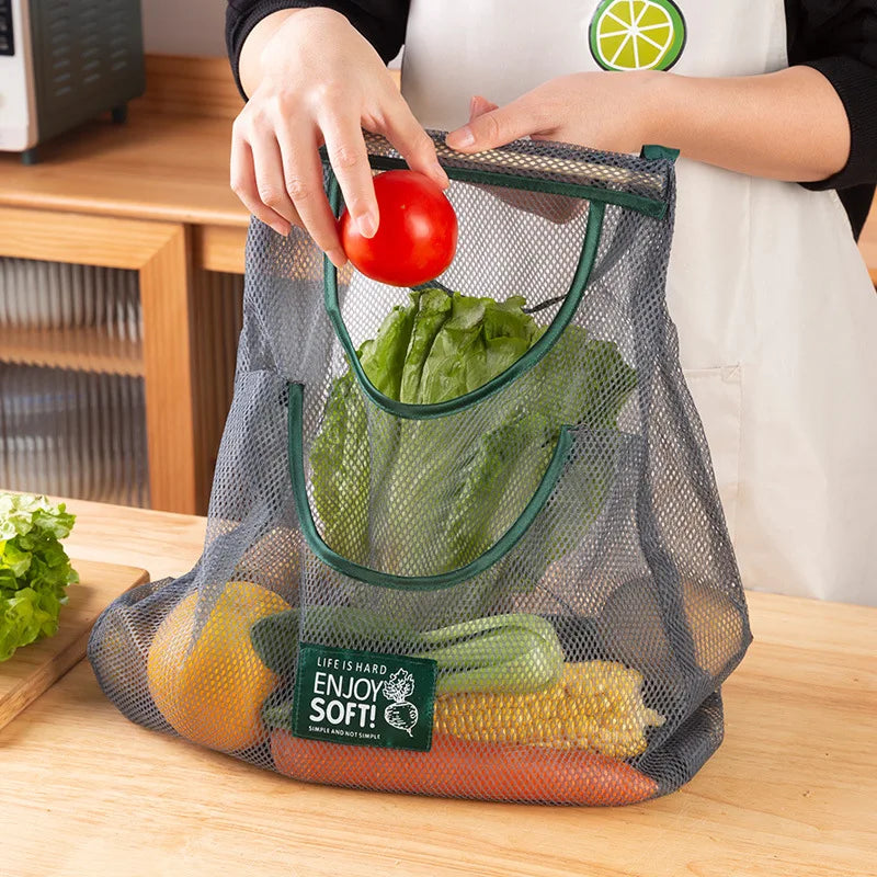 Person placing a tomato into a mesh produce bag filled with vegetables on a wooden surface.