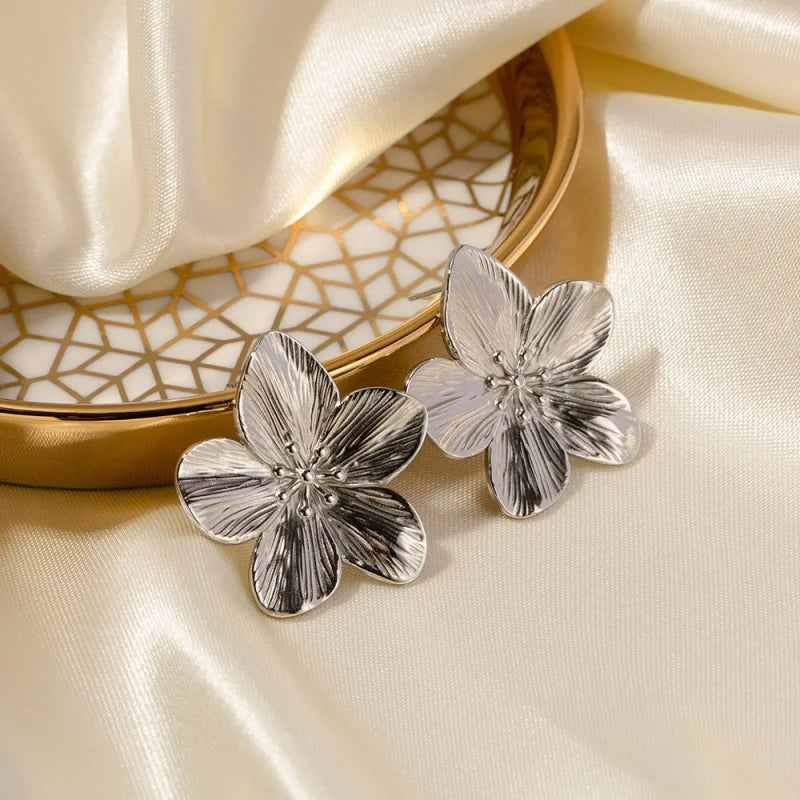 Silver floral earrings on a beige fabric background