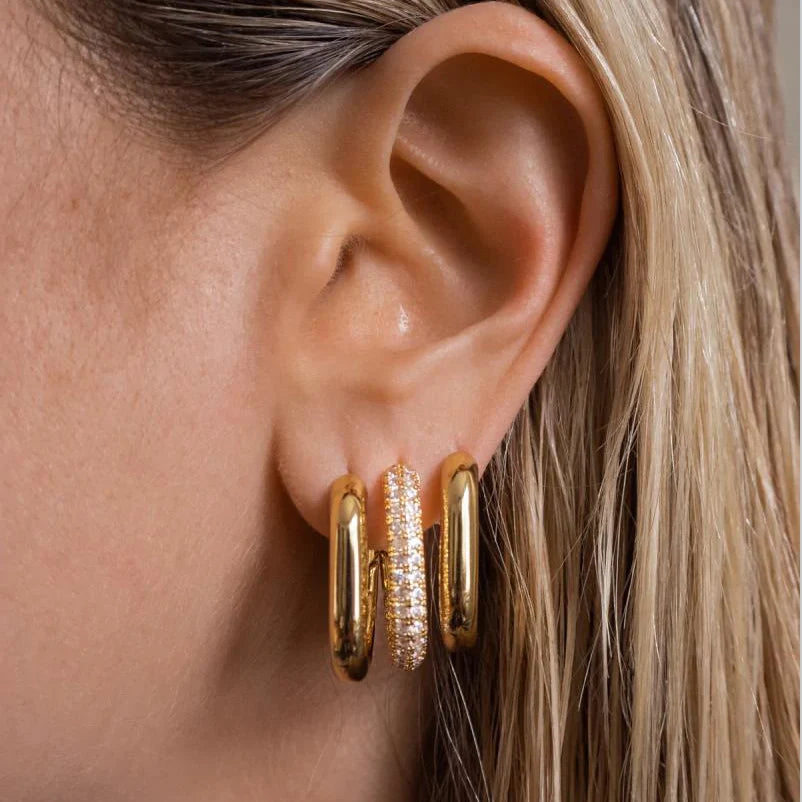 Close-up of an ear wearing gold hoop earrings with a blurred background