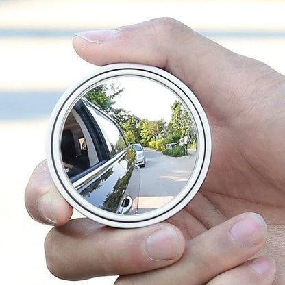 Hand holding a small round mirror reflecting a road scene with trees and vehicles.