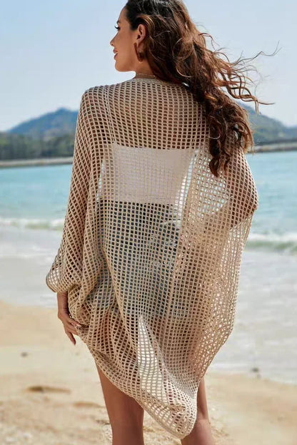 Woman wearing a beige mesh cover-up on a beach with ocean and mountains in the background