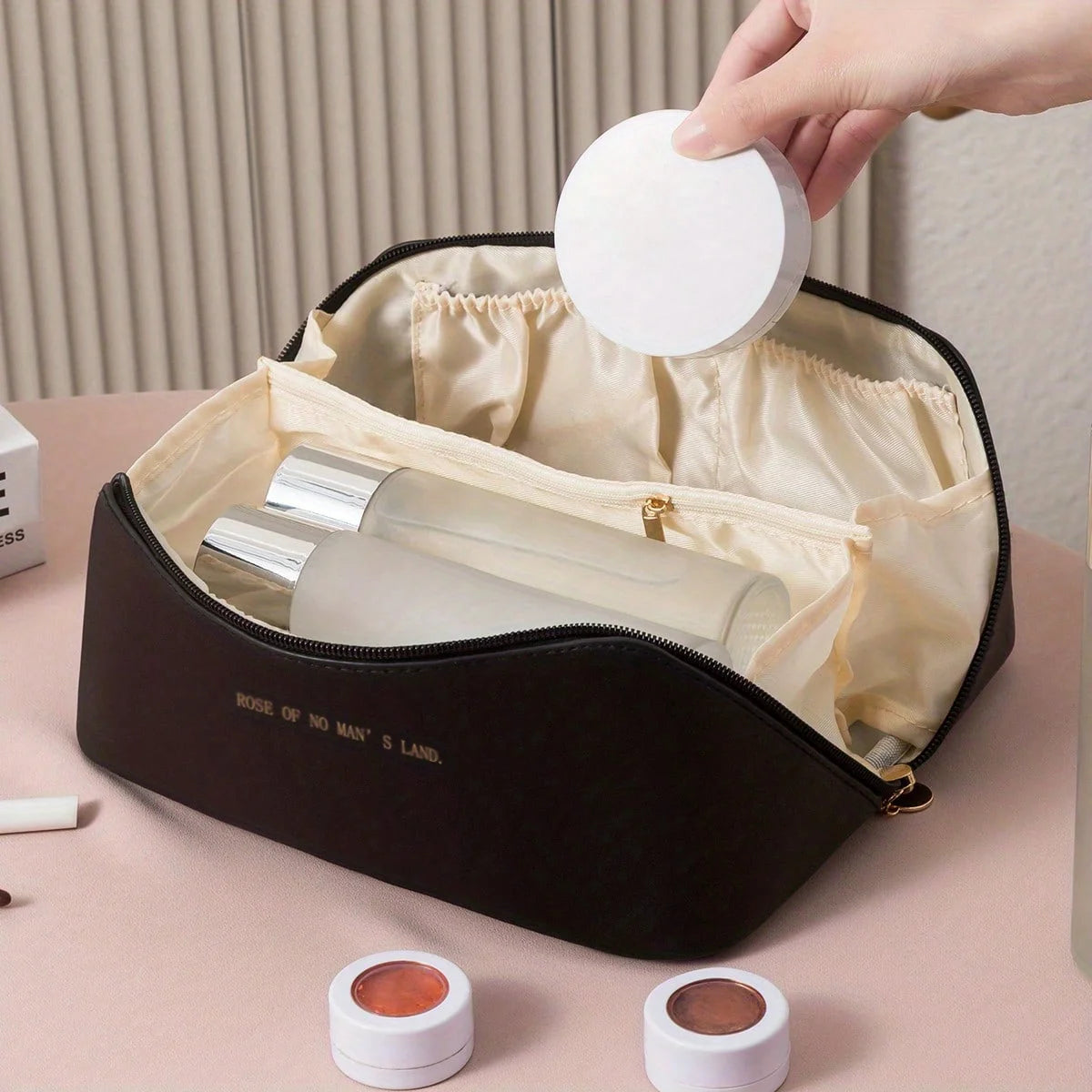 Black cosmetic bag with makeup items on a pink surface