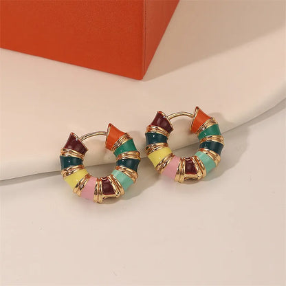 Colorful hoop earrings with gold accents on a beige surface.