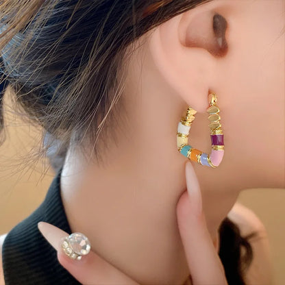 Close-up of a person wearing colorful hoop earrings with gold accents.