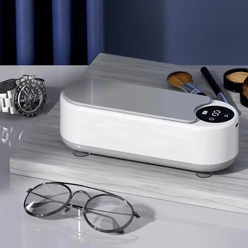 White electronic device on a wooden surface with glasses and makeup items in the background