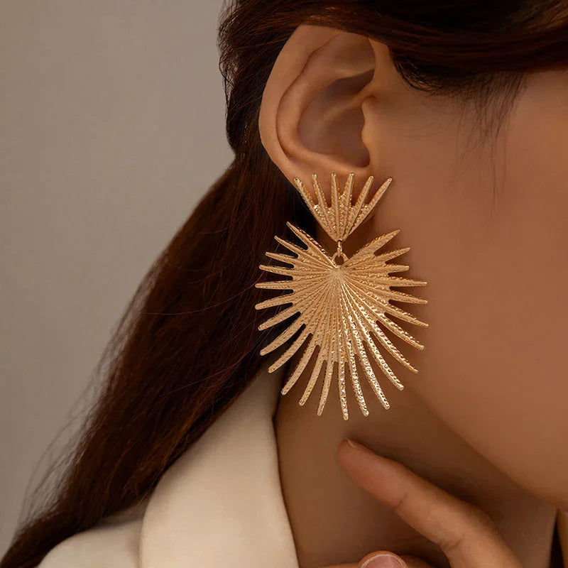 Gold earrings worn by a person with a neutral background