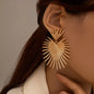 Gold earrings worn by a person with a neutral background