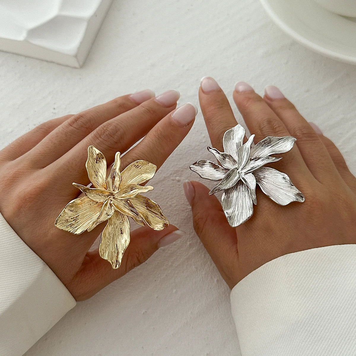 Gold and silver floral rings on a person's fingers against a neutral background