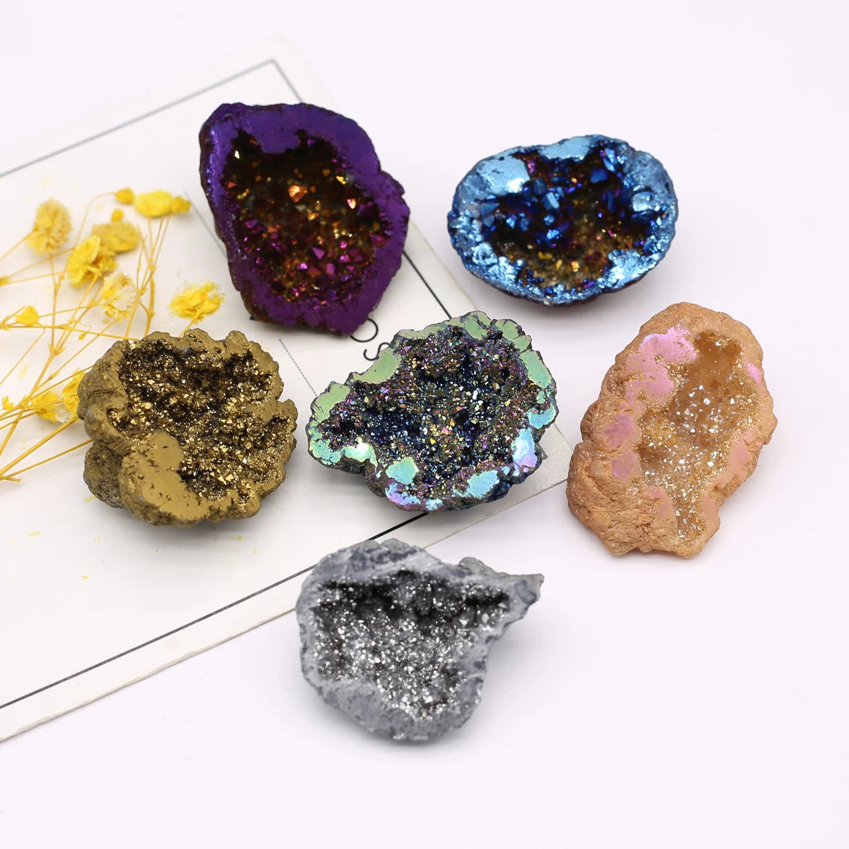 Collection of colorful geode crystals on a white surface with yellow flowers.