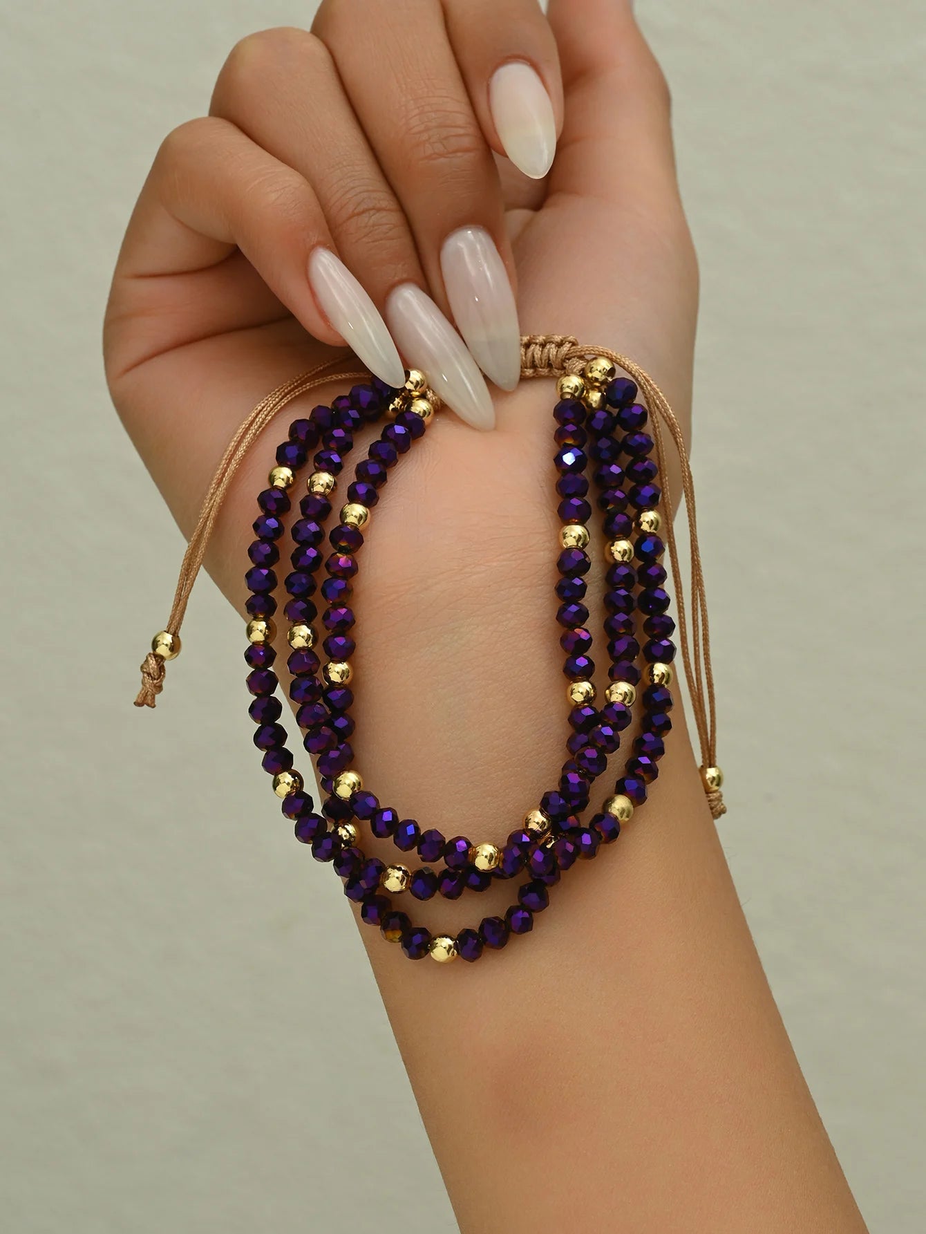 Hand wearing a stack of purple beaded bracelets on a neutral background