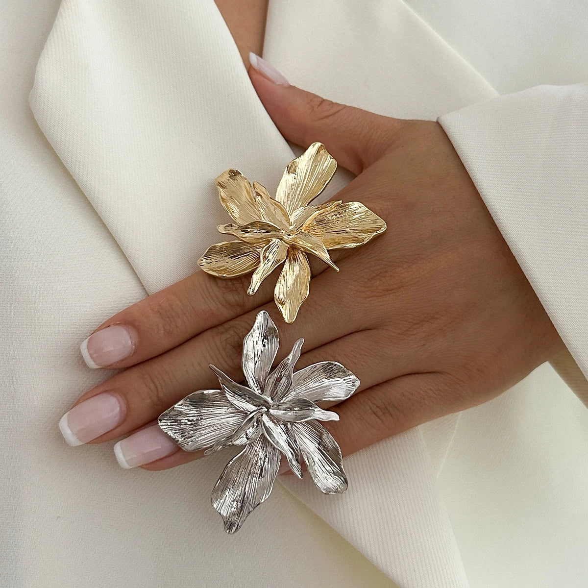 Gold and silver floral earrings on a hand against a white background