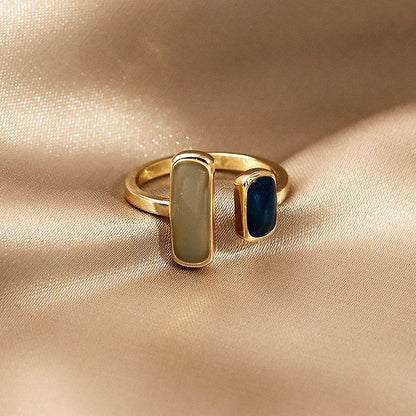 Gold ring with two colored stones on a beige fabric background