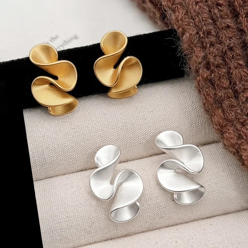 Gold and silver earrings on a jewelry display with a textured surface.