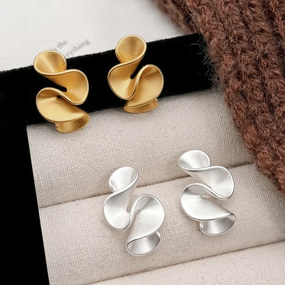Gold and silver earrings on a jewelry display with a textured surface.