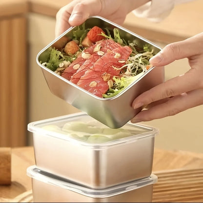 Stainless steel lunch box with salad and meat being held above it on a wooden surface.