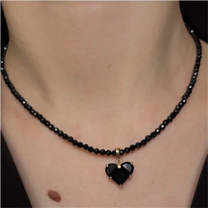 Black beaded necklace with a heart-shaped pendant on a person's neck
